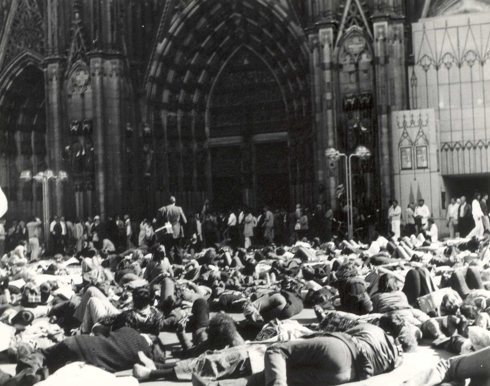 Demonstrant*innen liegen auf dem Domplatz, andere Aktivist*innen und Zuschauer*innen stehen am Rande des Platzes und vor dem Eingangsportal des Kölner Doms