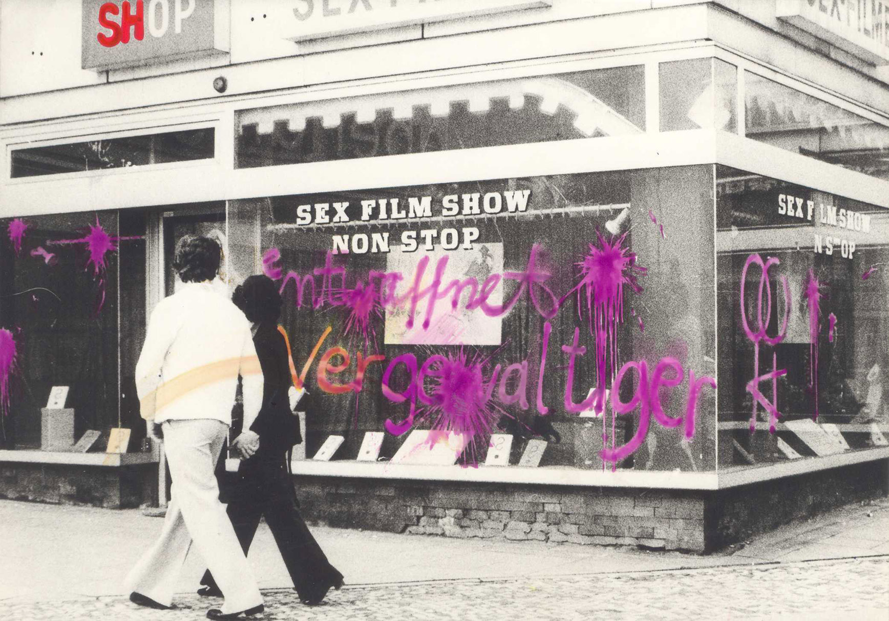 Graffiti in roter Farbe mit der Aufschrift „Entwaffnet Vergewaltiger“ und diverse aufgesprayte Frauenzeichen auf der Schaufensterscheibe eines Sex-Shops mit der Reklame „Sex Film Show Non Stop“; ein Paar geht händchenhaltend an dem Laden vorbei