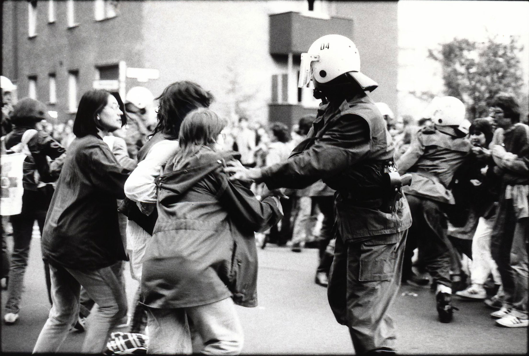 Polizisten in Schutzanzügen mit Helmen drängen Demontrantinnen von der Straße