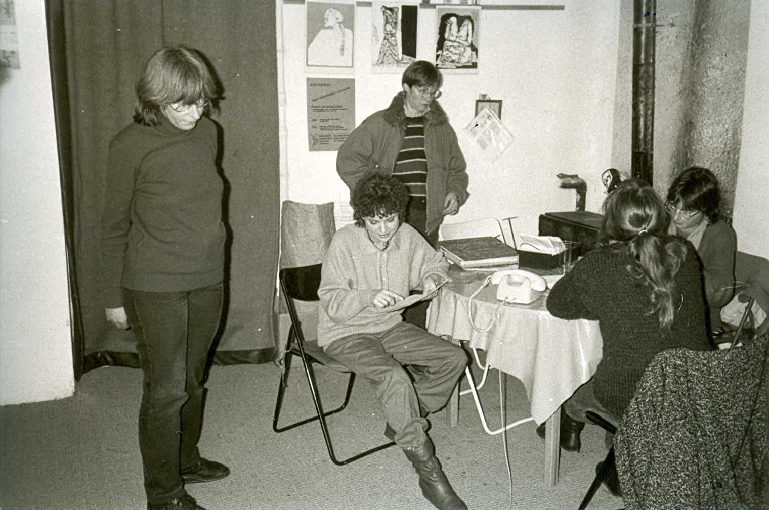 Fünf FFBIZ-Mitfrauen u.a. Ursula Nienhaus und Monika Barba im Gespräch während eines Plenums im Frauenladen; im Hintergrund Vorhang vor Tür oder Durchgang, Ofen mit langem Ofenrohr und Alufolie dahinter