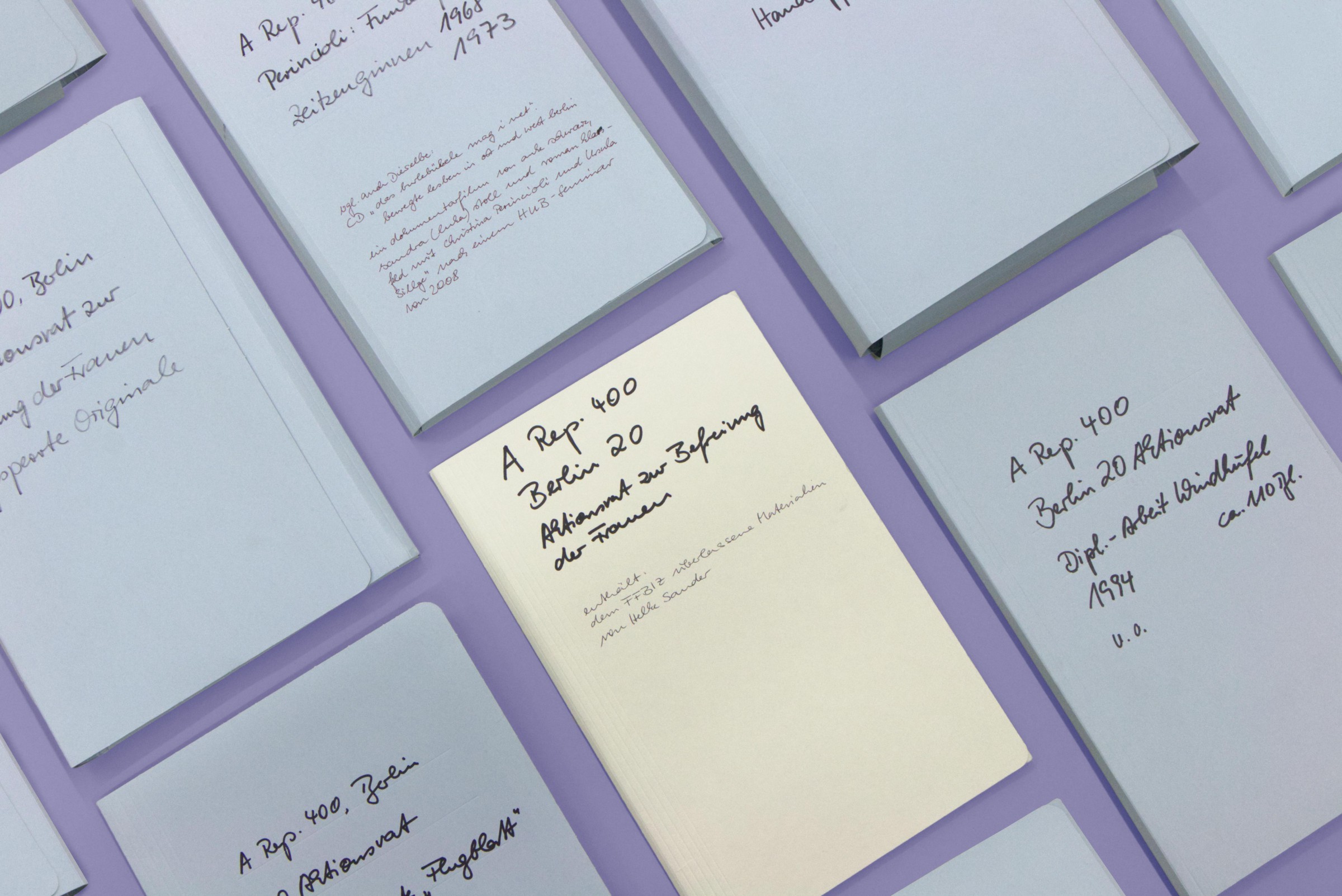 diverse beschriftete Archivmappen mit Unterlagen des Aktionsrates zur Befreiung der Frauen vor lila Hintergrund